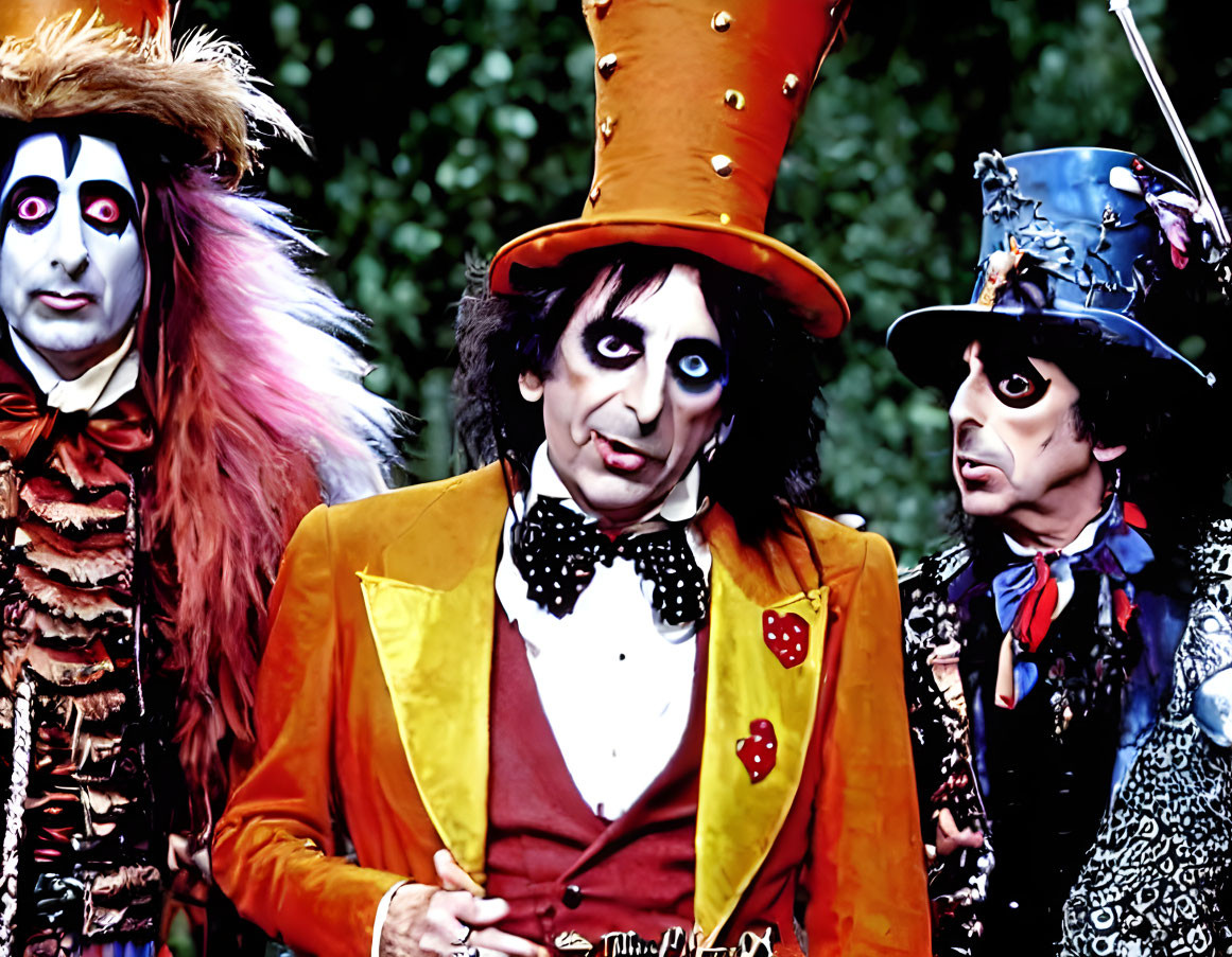 Three individuals in colorful whimsical costumes with theatrical makeup.