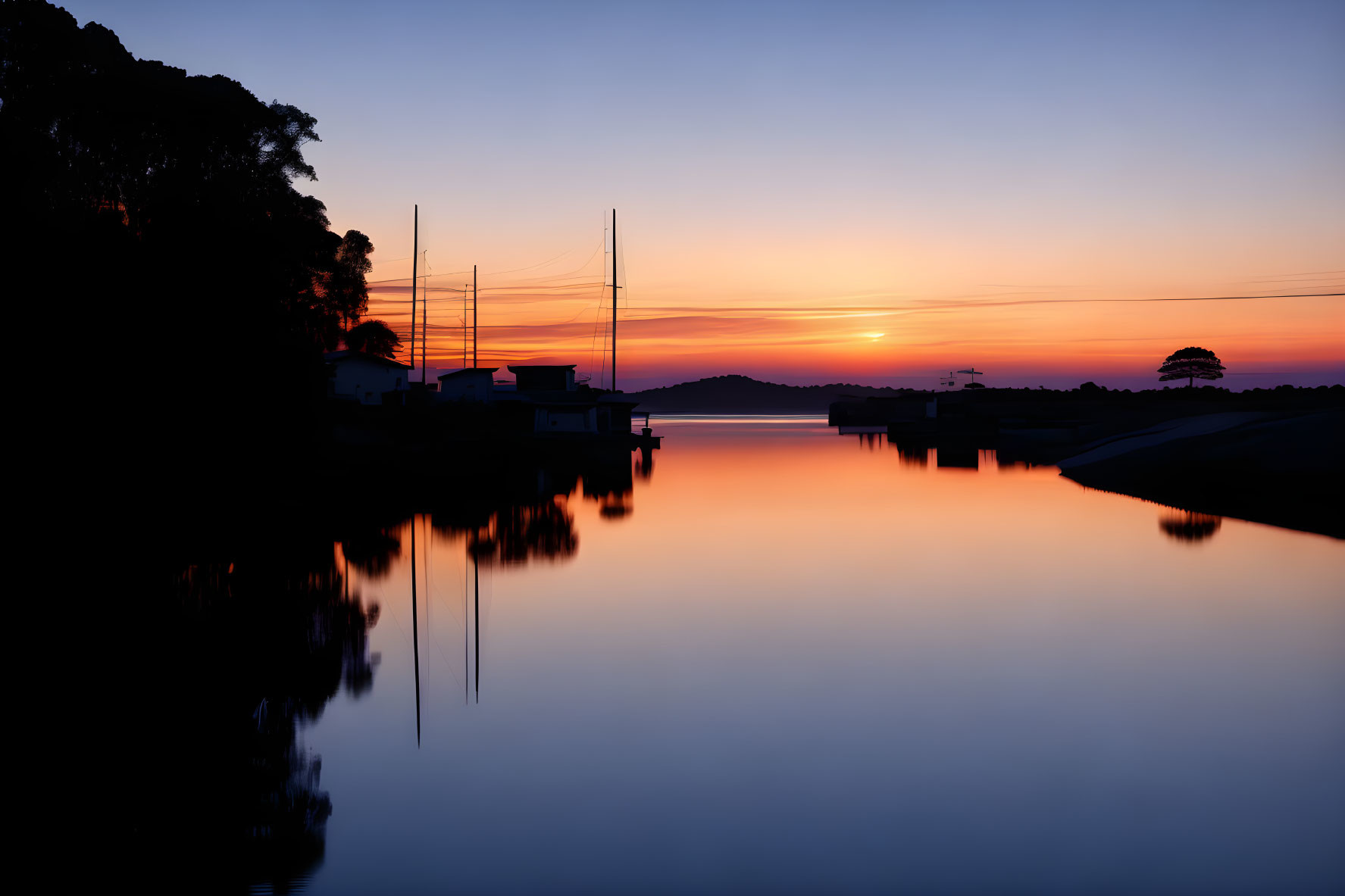 Tranquil sunset with vivid orange hues reflected on water and silhouetted trees.