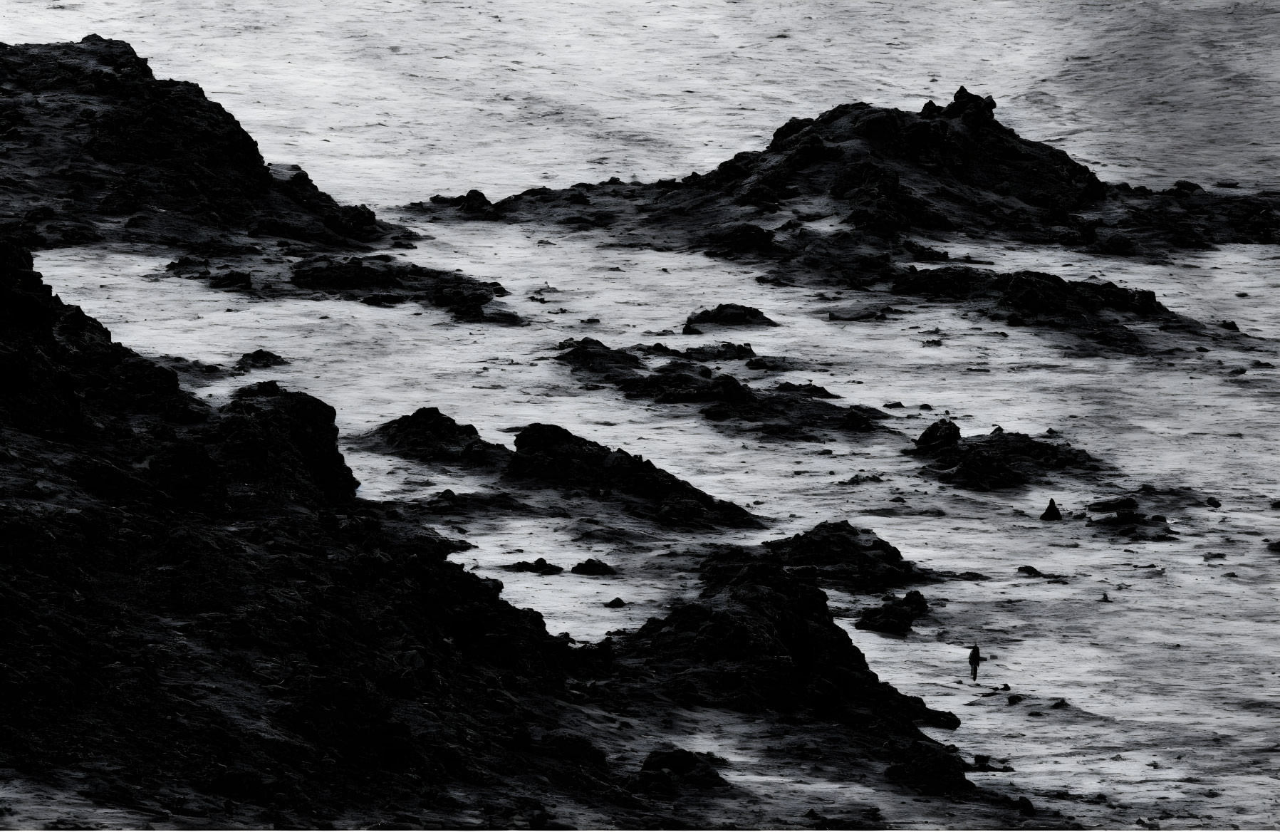 Monochrome image of rugged coastline with figure and crashing waves