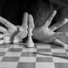 Monochrome image of person with multiple arms playing chess on checkered board