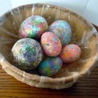 Elaborately horned small dragon in decorative bowl with patterned eggs on embroidered surface