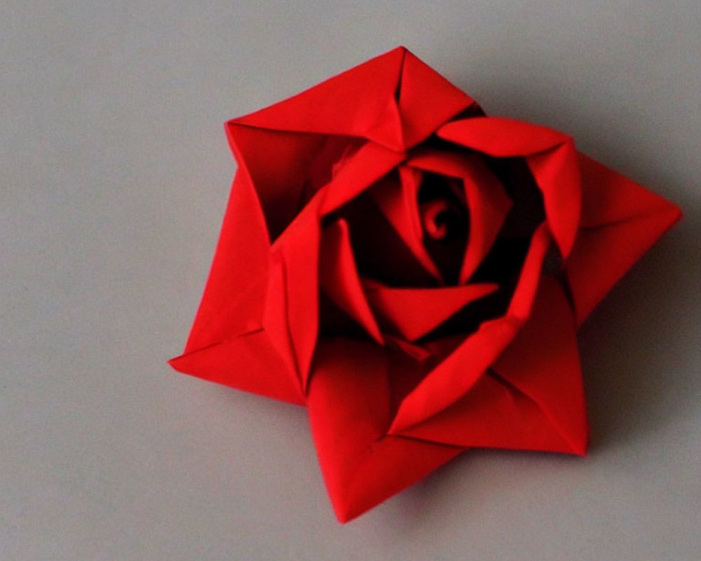 Vibrant red origami rose on light grey background