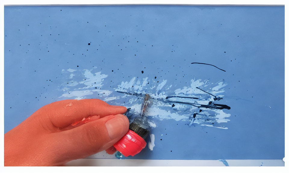 Hand squeezing black paint onto brush on blue paper with splatters