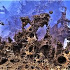 Cloaked figure in desert with jagged rocks under blue sky