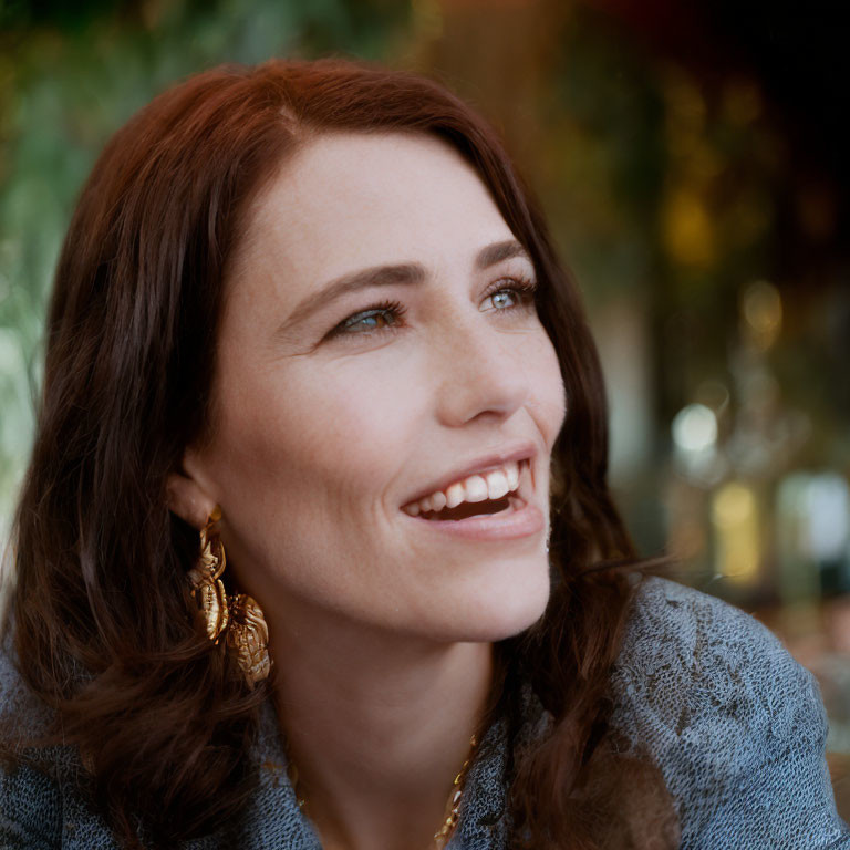 Smiling woman with brown hair in gold earrings and gray knit top