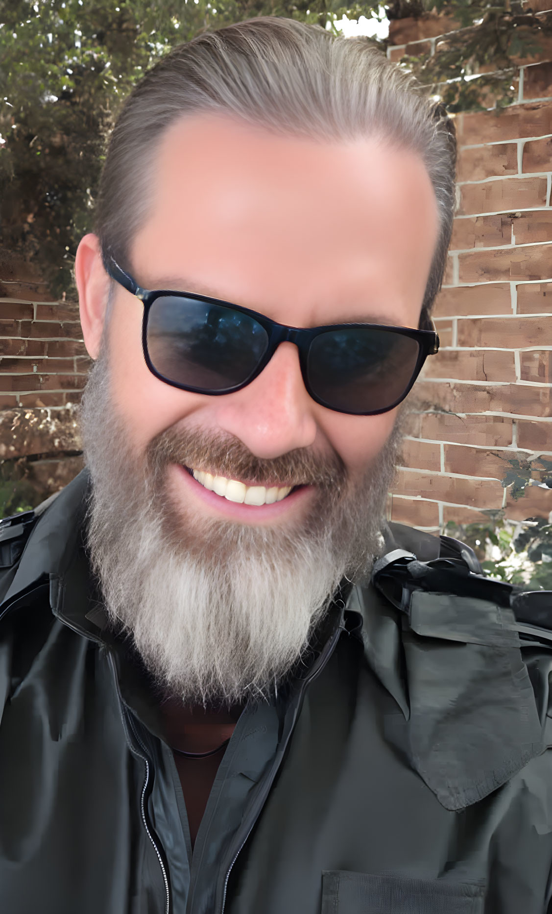 Bearded man in sunglasses smiling against brick wall