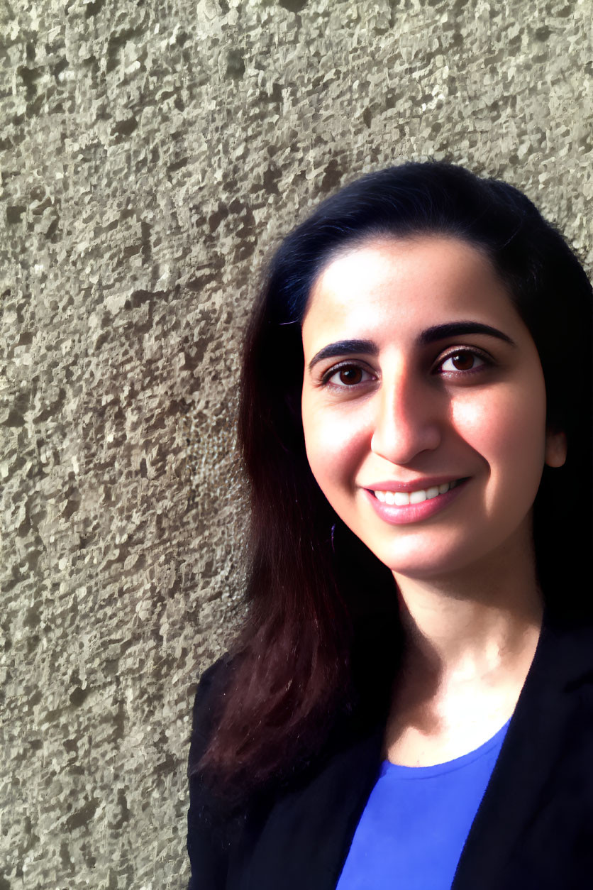 Smiling woman in black jacket against textured beige wall