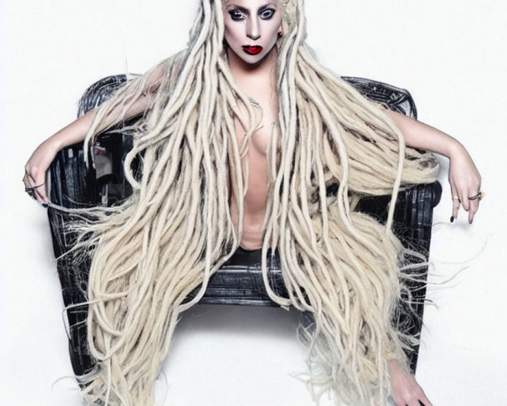 Portrait of a person with long white dreadlocks and bold makeup sitting in a black chair