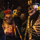 Stylized skeletons with hats and flowers in Day of the Dead theme against dark tunnel.