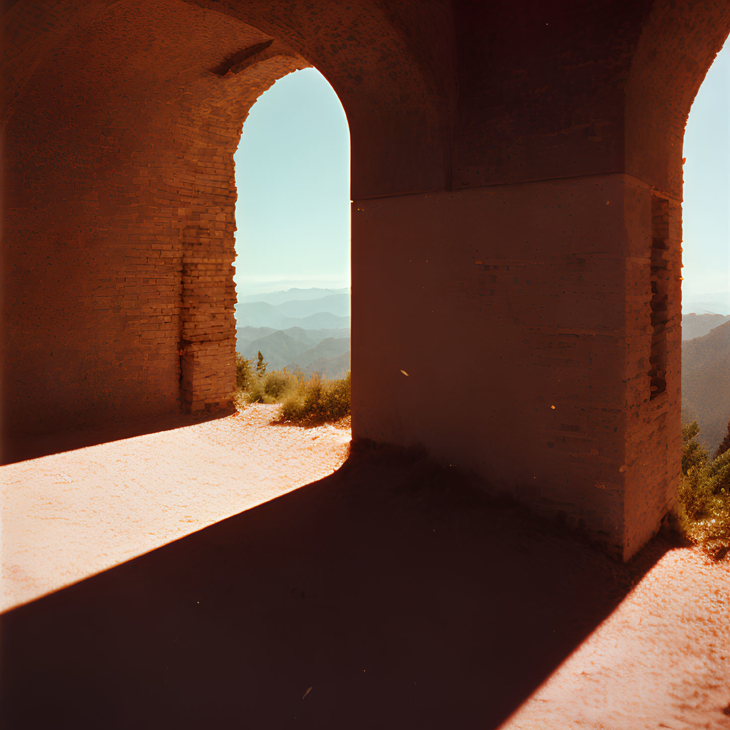 Arched brick structure casting shadows with view of mountain range under clear sky