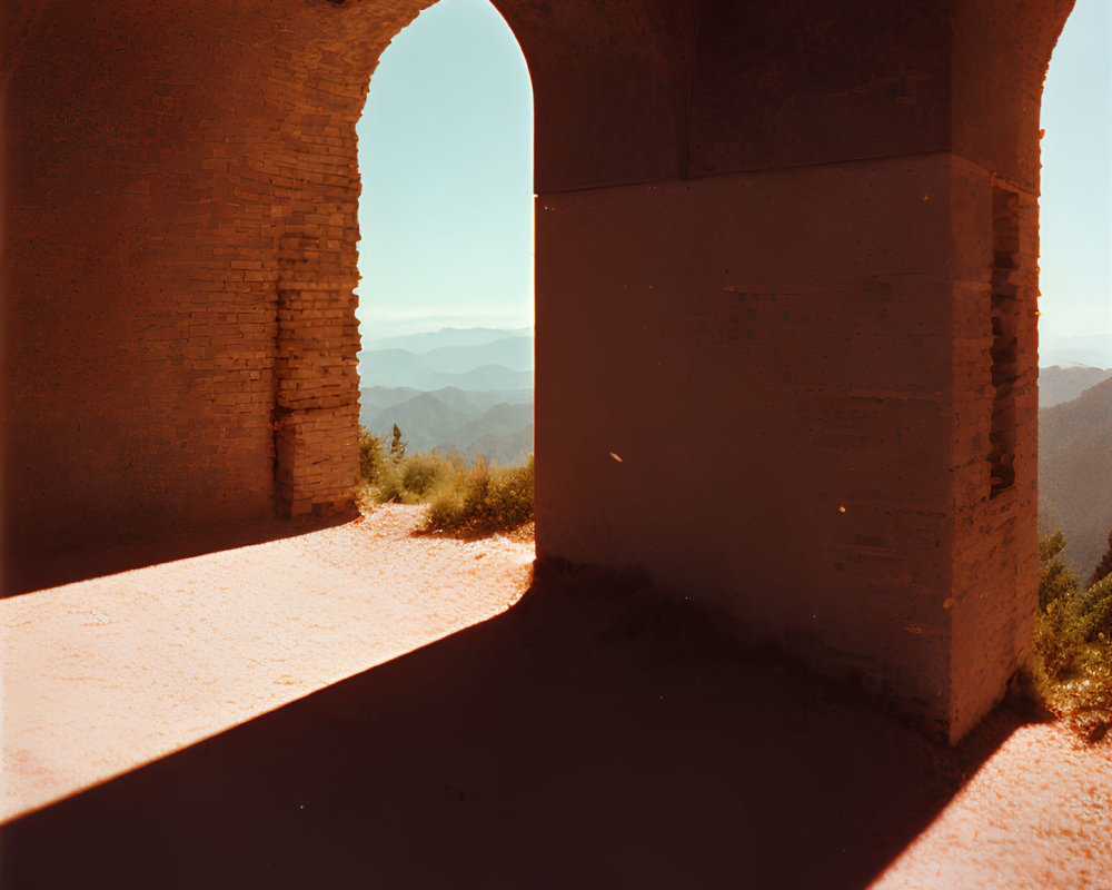 Arched brick structure casting shadows with view of mountain range under clear sky