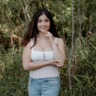 Long-haired woman in white crop top and jeans amidst greenery.