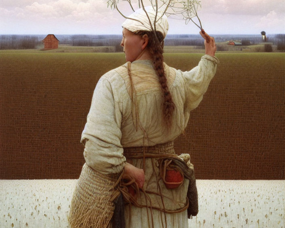 Traditional attire woman holding sprig in field with farmhouse in background