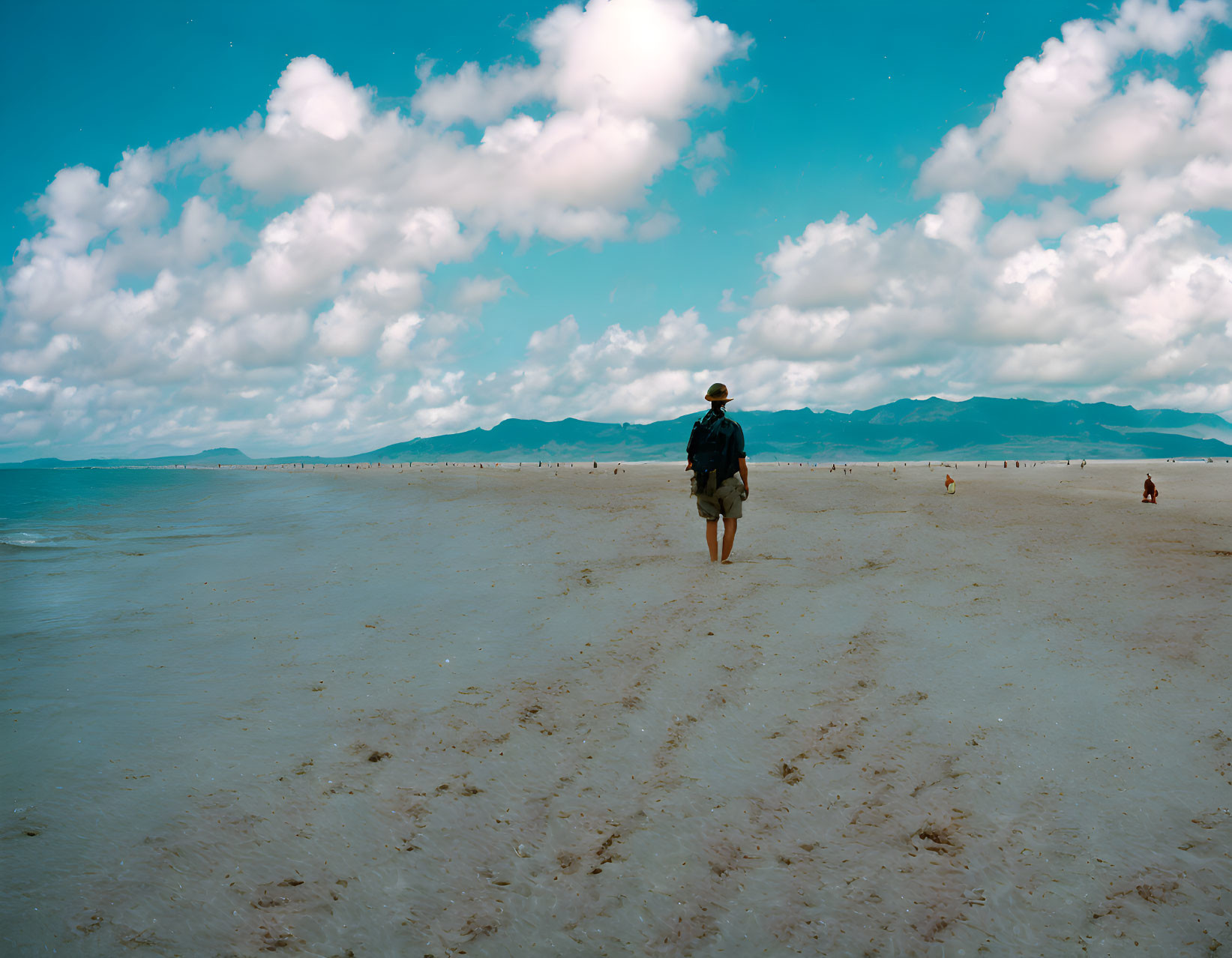 Sunny beach with white sand, blue sky, clouds, and mountains