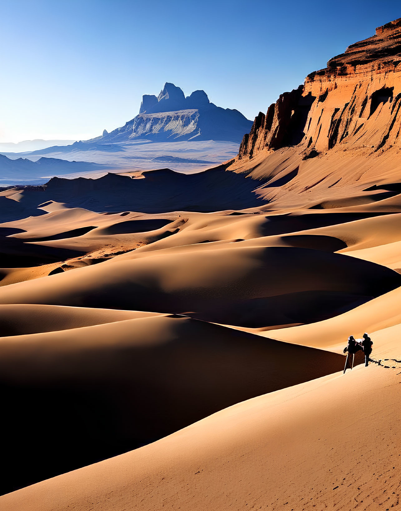 Scenic image of people looking at sand dunes and mountain under blue sky