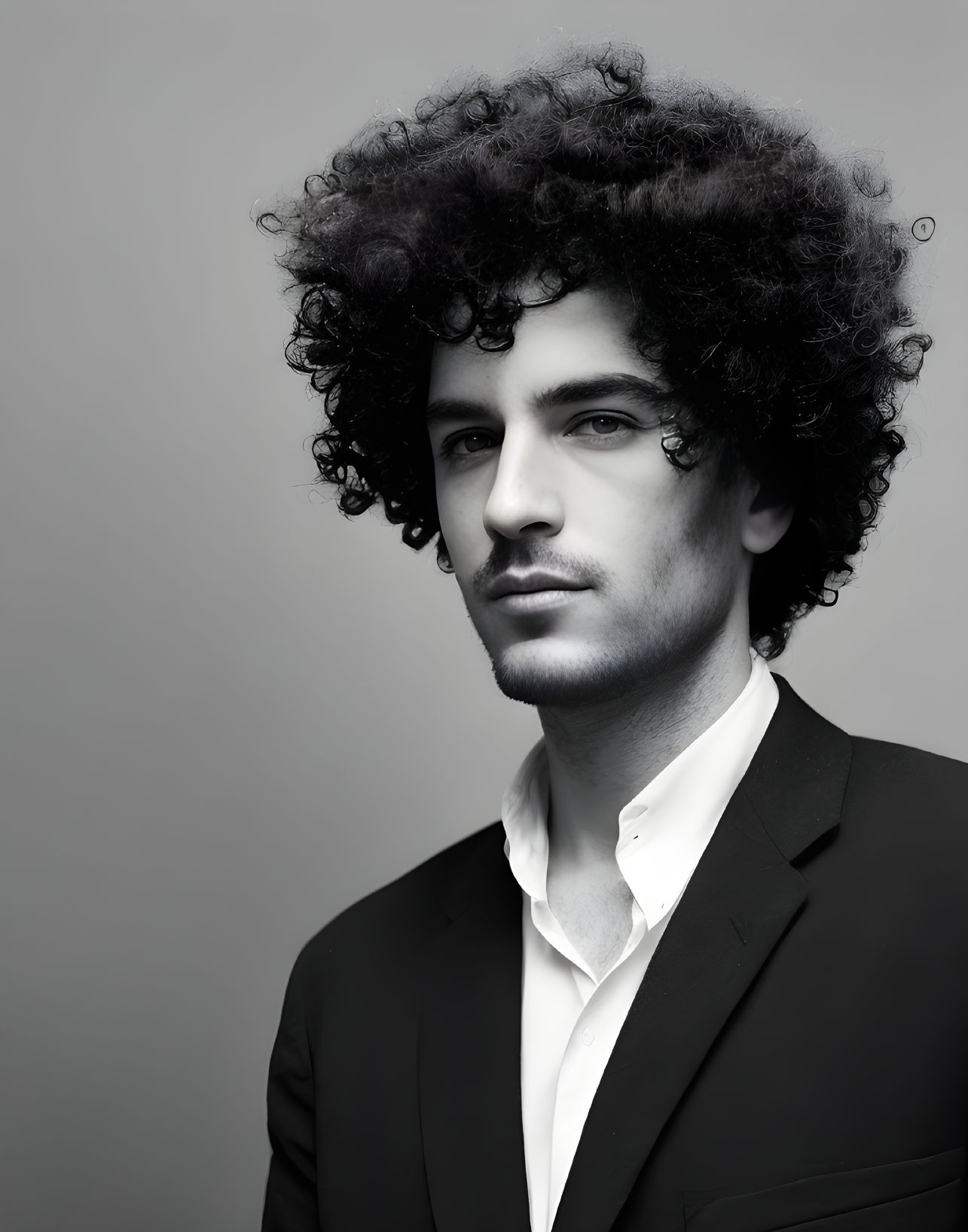 Monochrome portrait of a man with curly hair in suit and white shirt