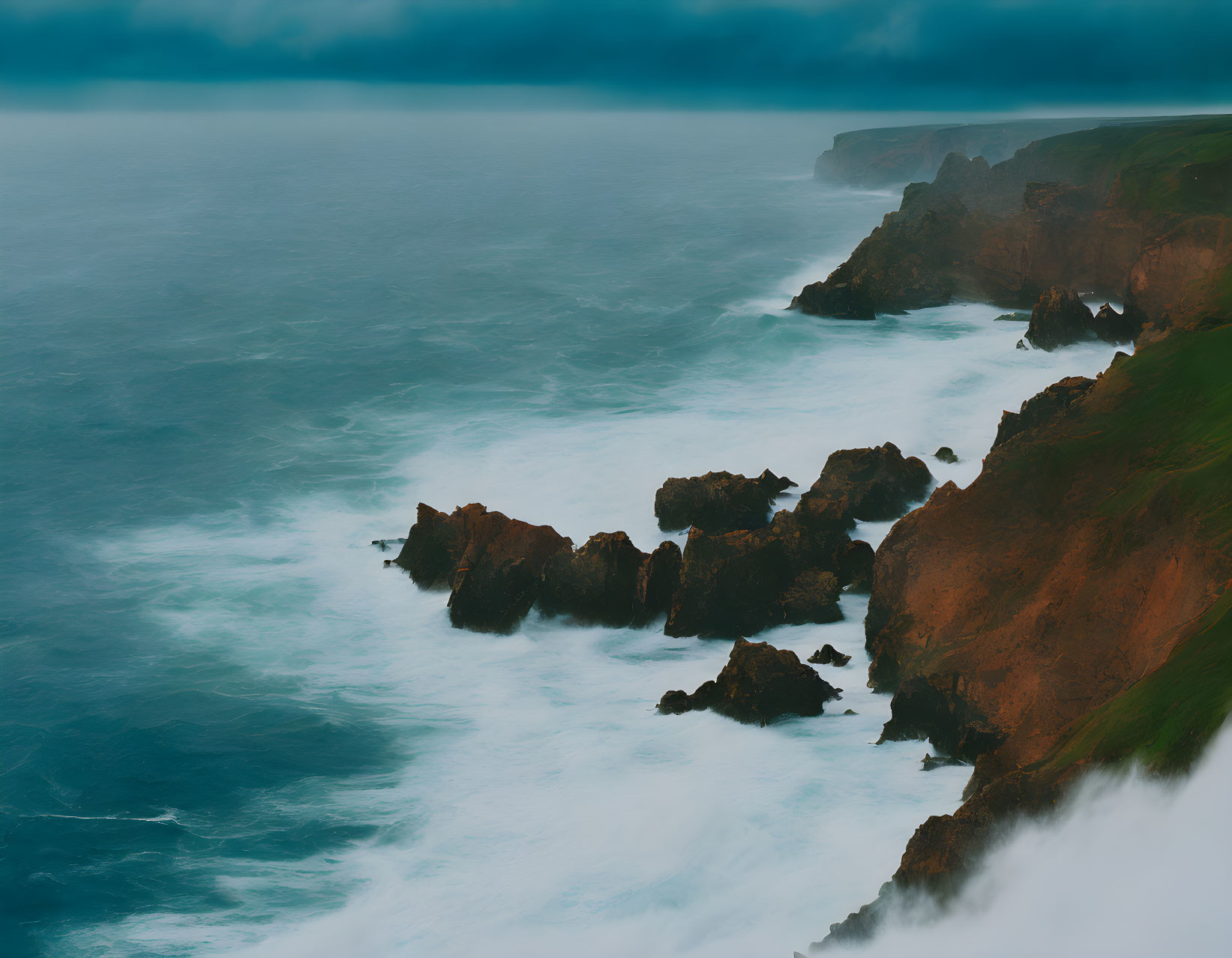 Stormy sky over misty ocean with waves crashing against rugged cliffs