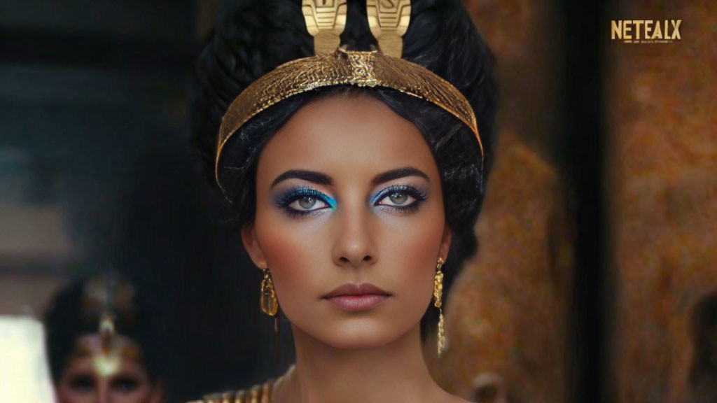 Elaborate Cleopatra styled woman with blue eye makeup and gold accessories.