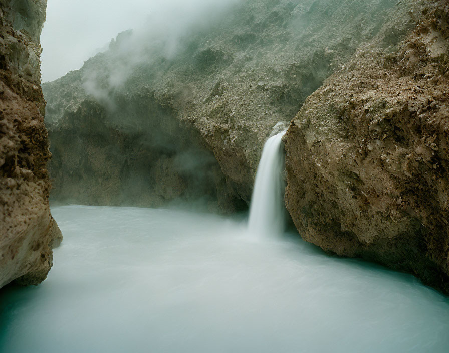 Tranquil waterfall cascading into misty pool surrounded by rugged rocks