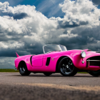 Pink classic convertible with exaggerated tailfins under dramatic cloudy sky