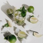 Realistic illustration: Glass of water with lemon, mint, ice on plate.