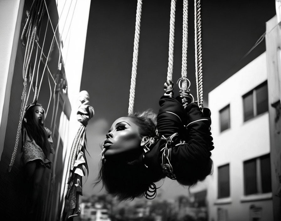 Monochromatic image of woman suspended by ropes against urban backdrop