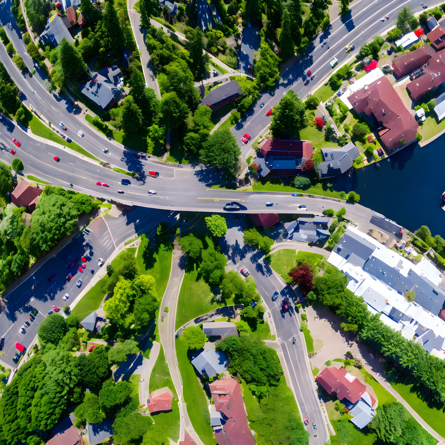 Sunny residential area with roads, vehicles, houses, and water.