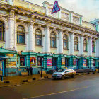 Historical building with large windows, blue canopies, wet streets, cars, and pedestrians.