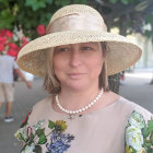 Woman with Striking Blue Eyes in White Hat and Floral Outfit on Mosaic Background