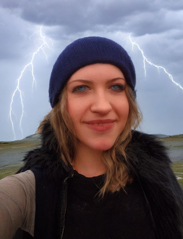 Smiling person in blue beanie with lightning in cloudy sky