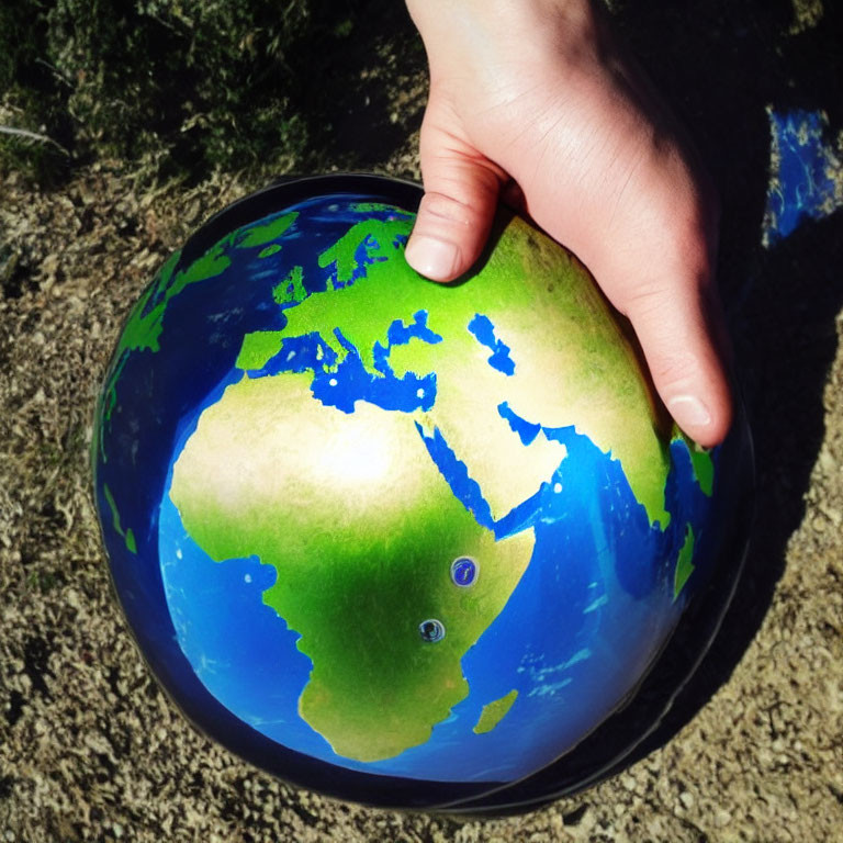 Hand holding globe with focus on North & South America, shadows accentuating contours