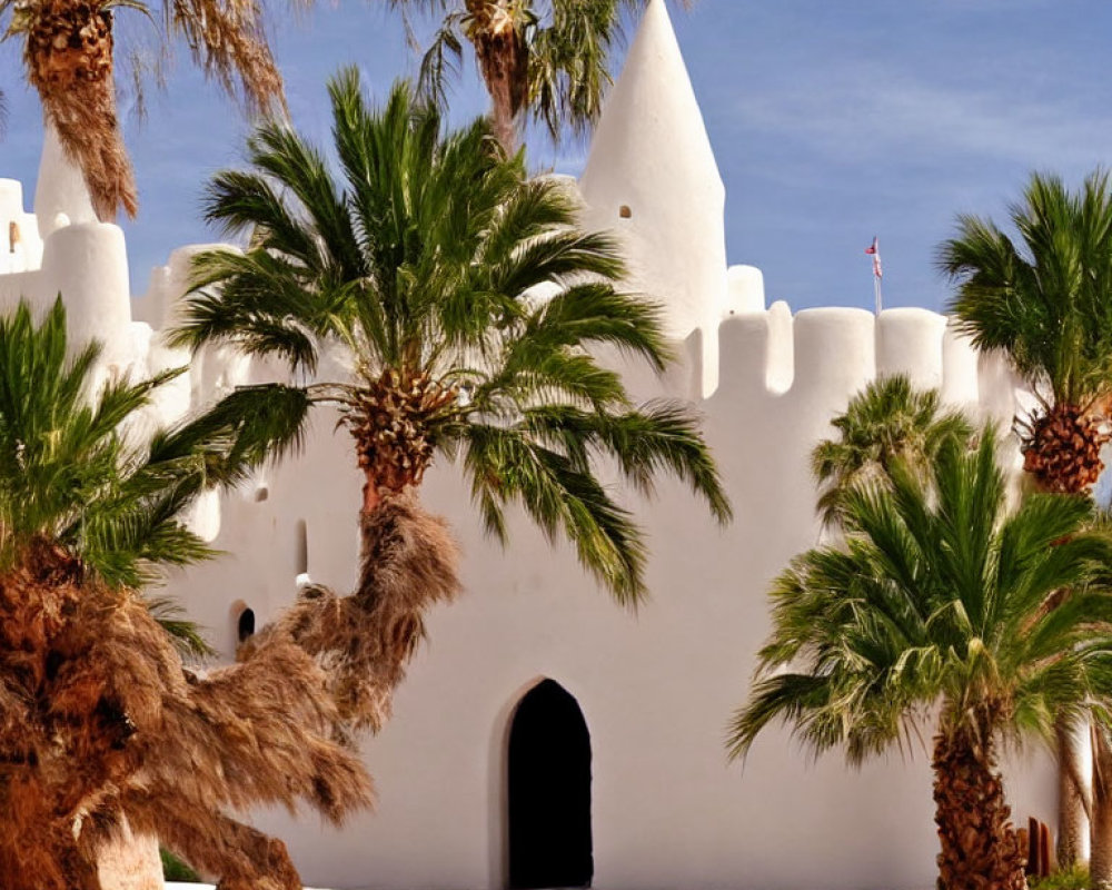 Traditional white-washed building with conical turrets and palm trees under clear blue sky