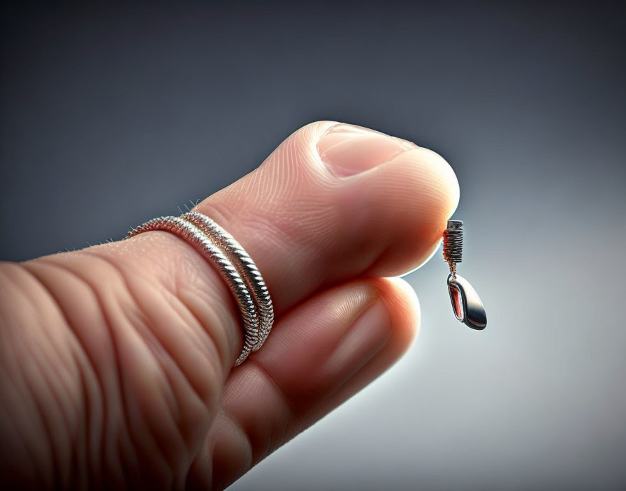 Metal coils around fingertip with floating eyeglass screw on gray background