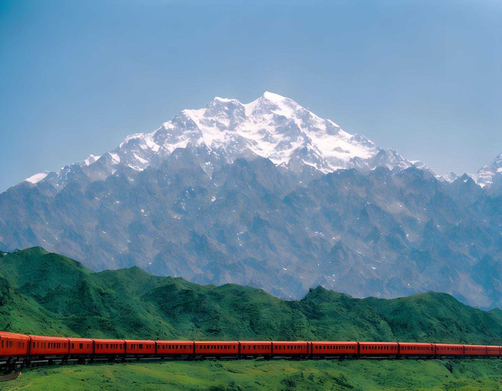 Red train in lush green foothills near snow-capped mountain