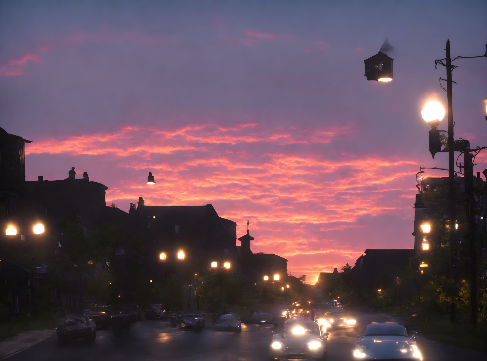 Vivid orange and pink sunset over suburban street with glowing streetlights and car headlights