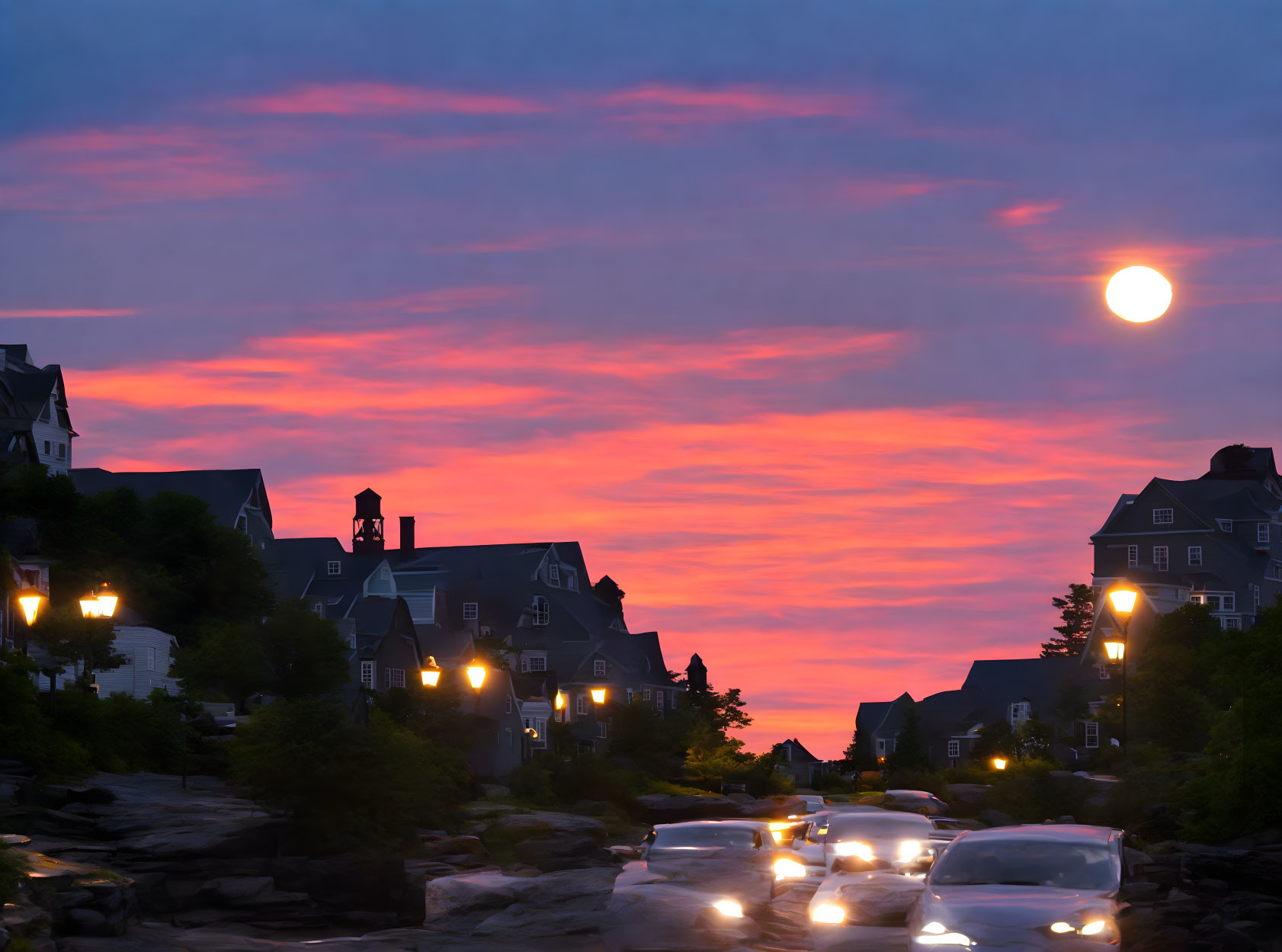 Charming coastal village at twilight with streetlamps, cars, and moonlit sky