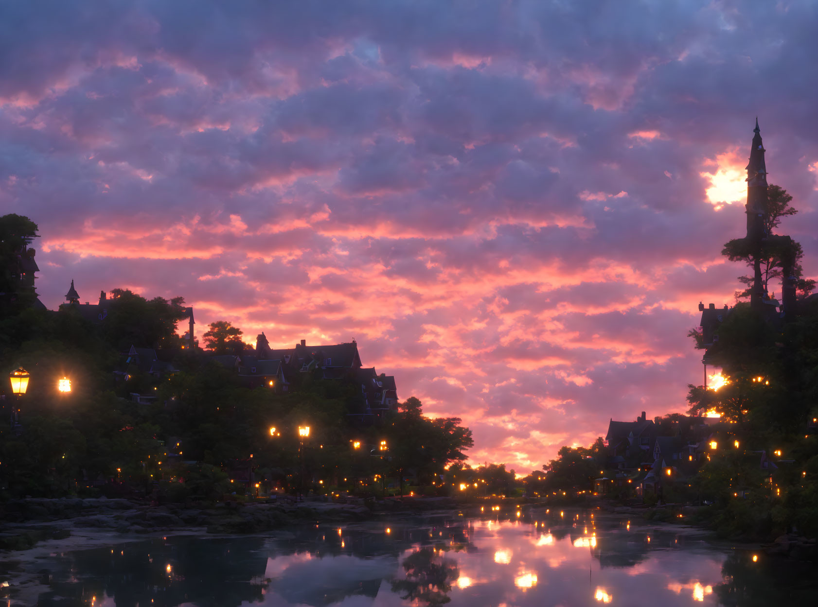 Tranquil town at dusk: illuminated street lamps, serene river, pink and purple sunset sky