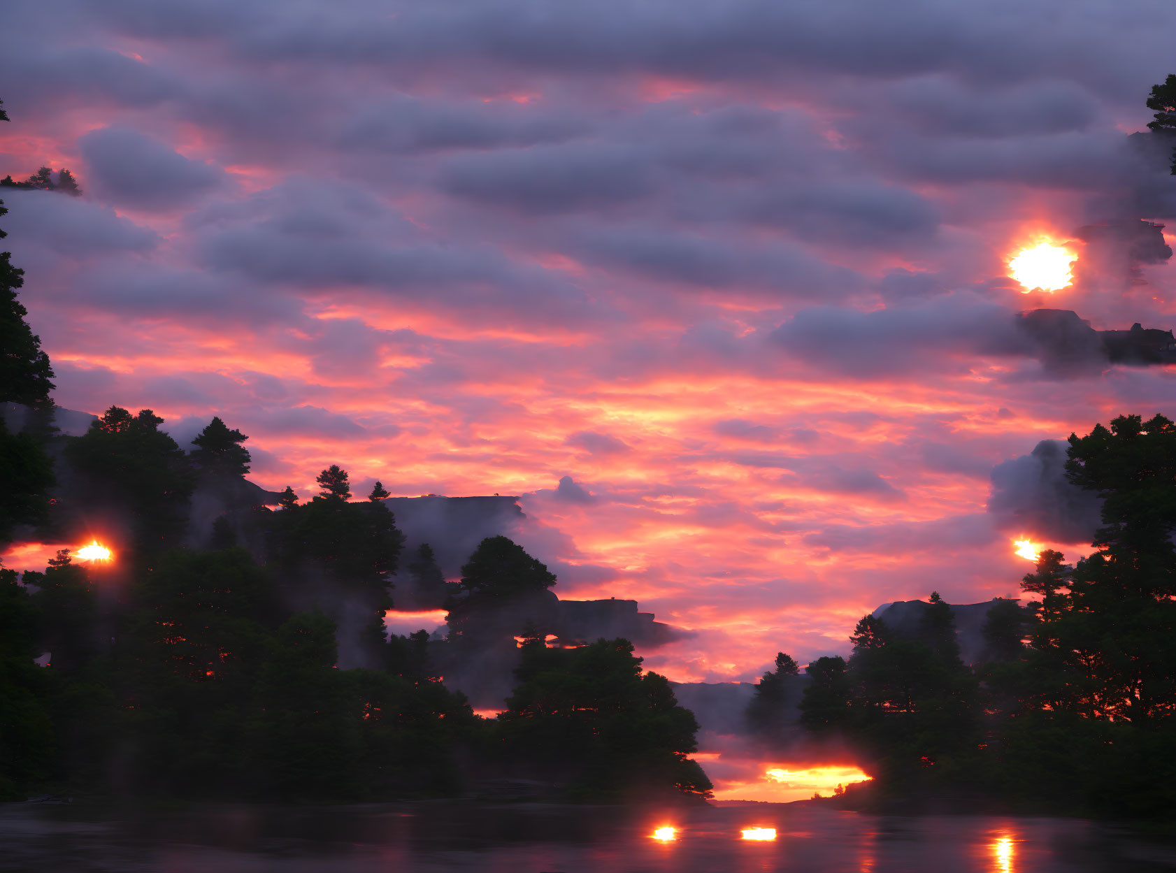 Vibrant pink and orange sunset over river with silhouetted trees and clouds