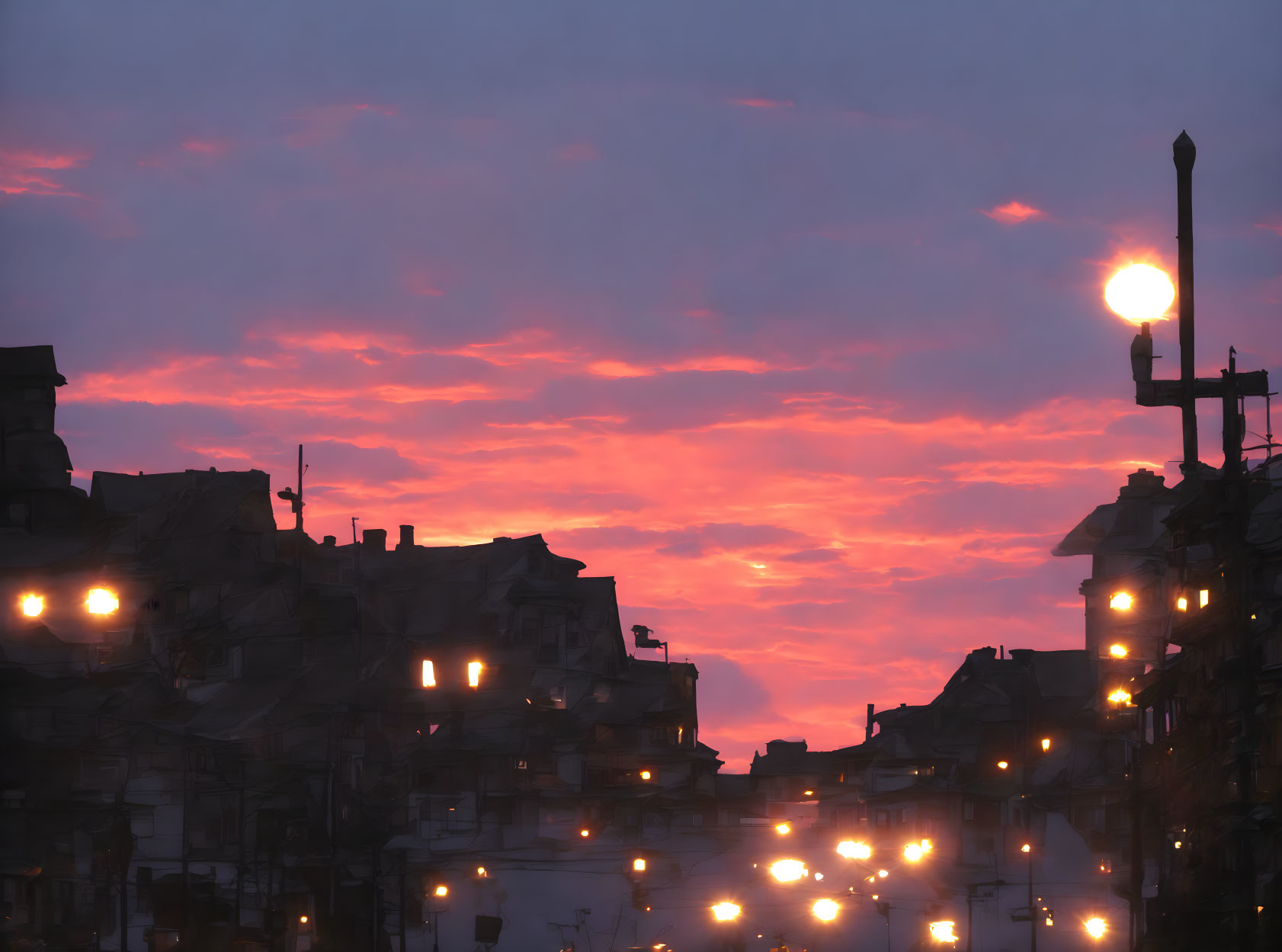 Cityscape at Dusk with Illuminated Buildings and Street Lamps under Vibrant Sky