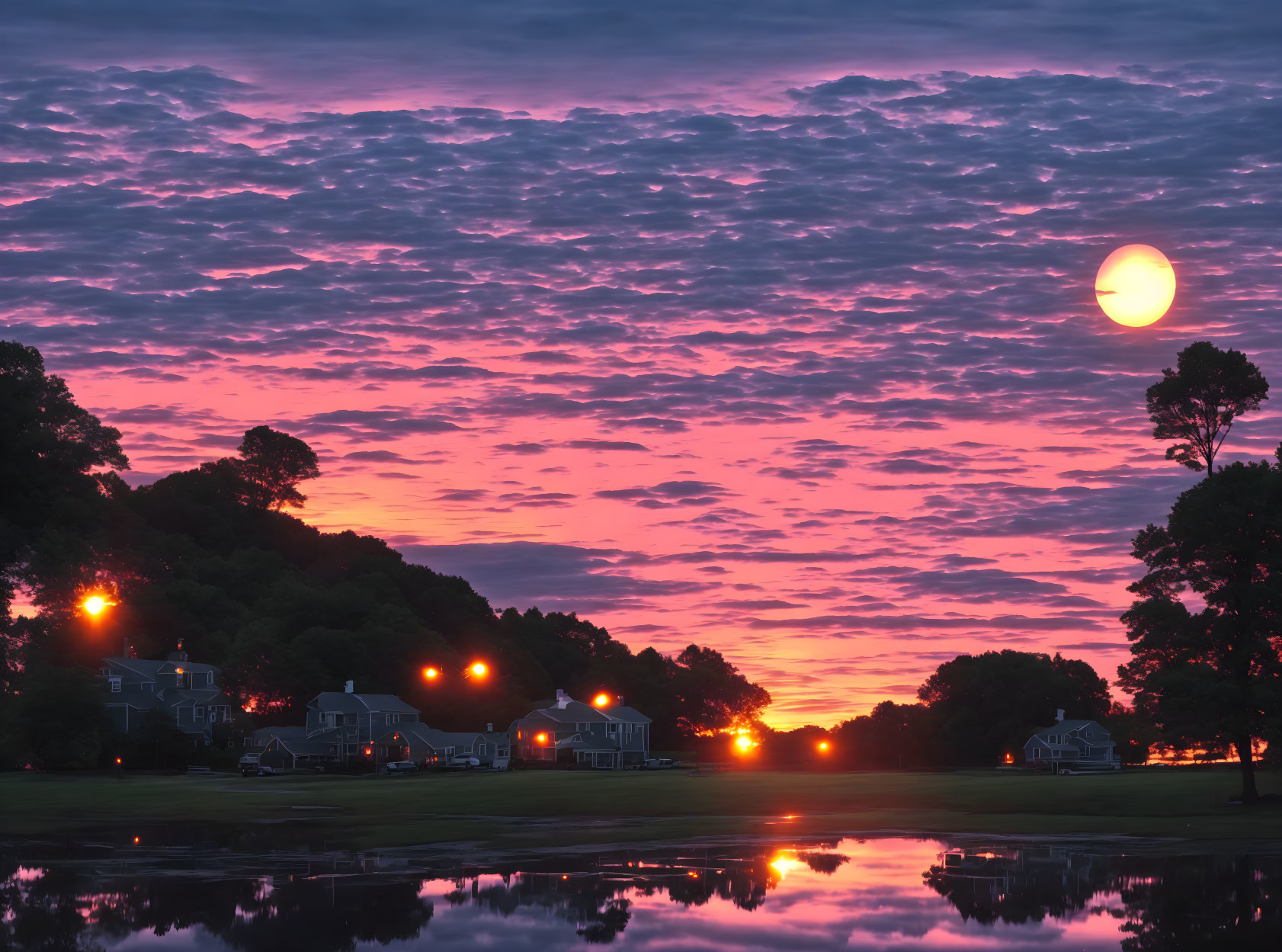 Colorful sunrise over peaceful neighborhood with calm lake and glowing streetlights