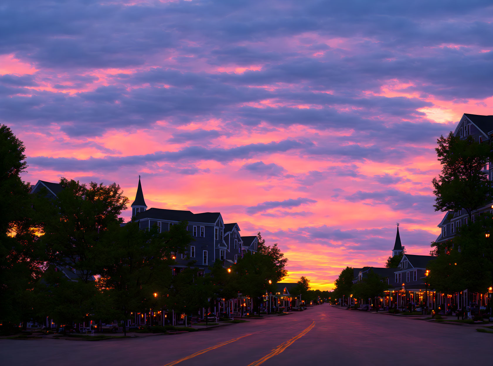 Colorful sunset over Victorian houses and streetlights with steeple in skyline