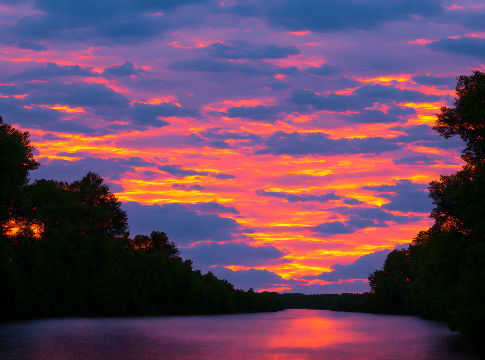 Vibrant sunset with orange clouds over serene river