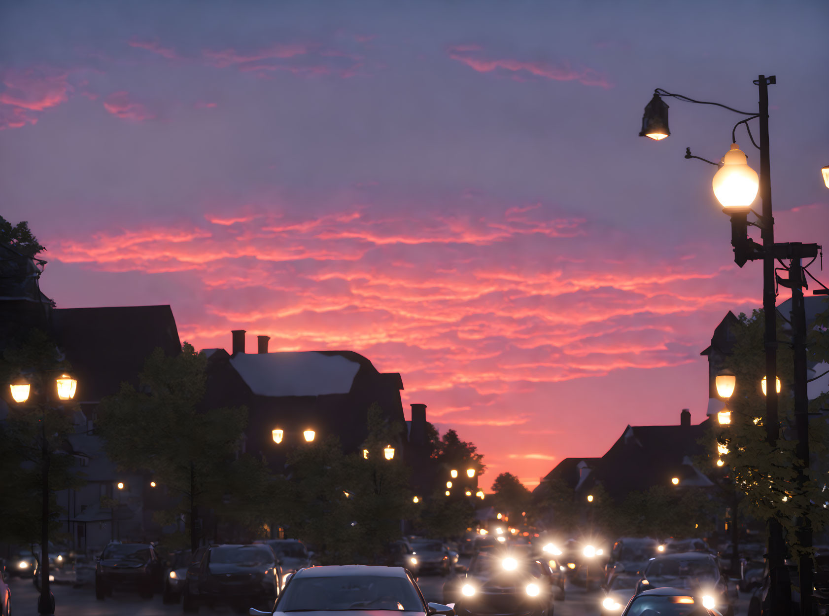 Colorful sunset over city street with cars, street lamps, and buildings