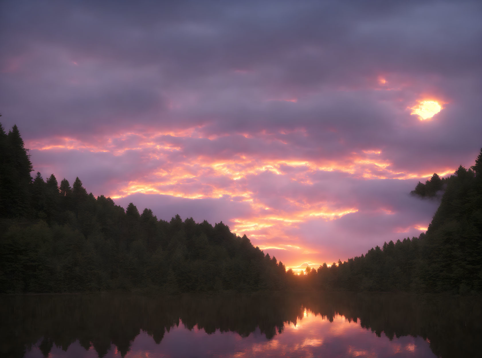 Tranquil lake at sunrise with pink and purple clouds reflecting in water