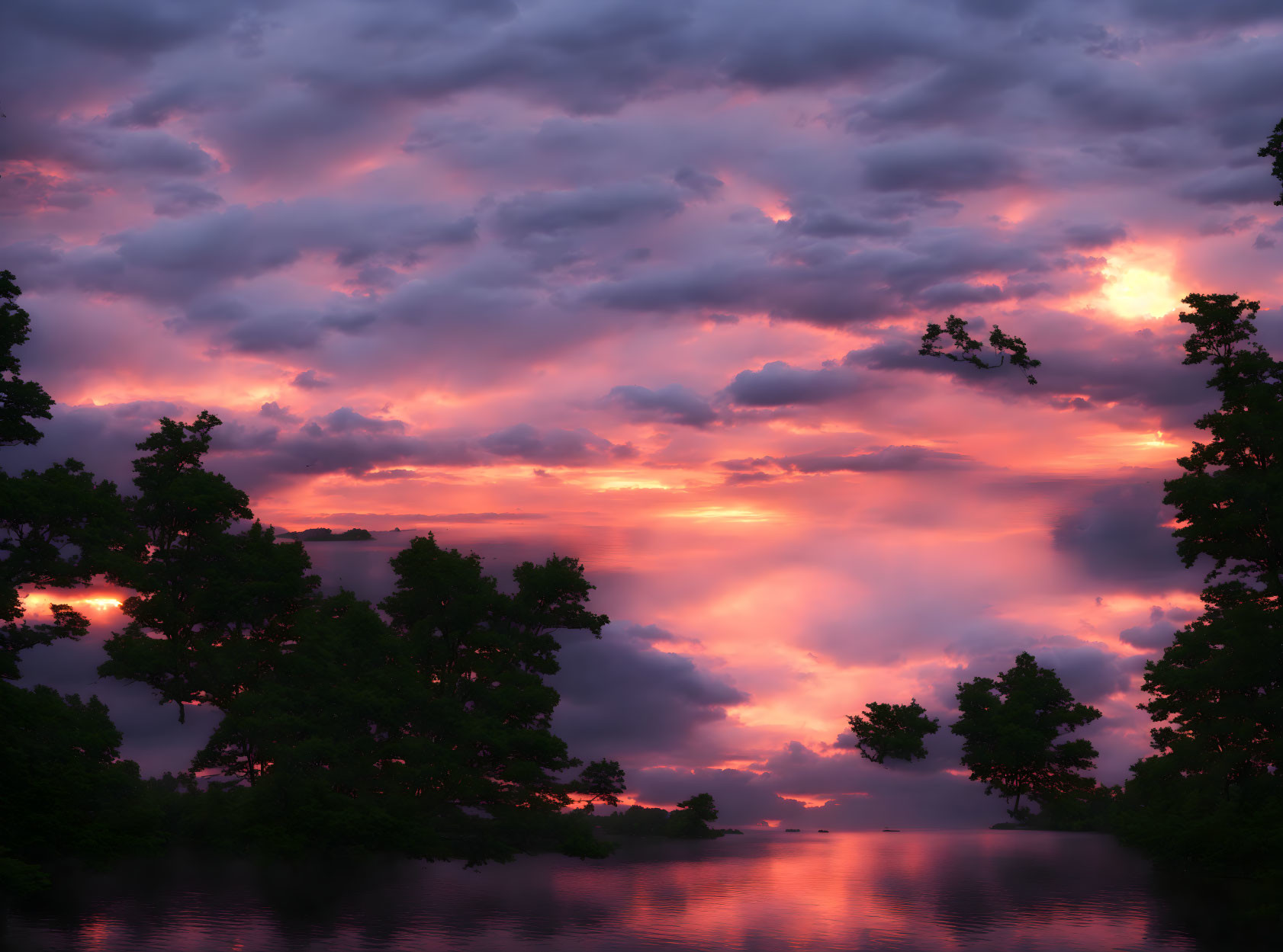 Fiery sunset reflected on tranquil water with silhouetted trees