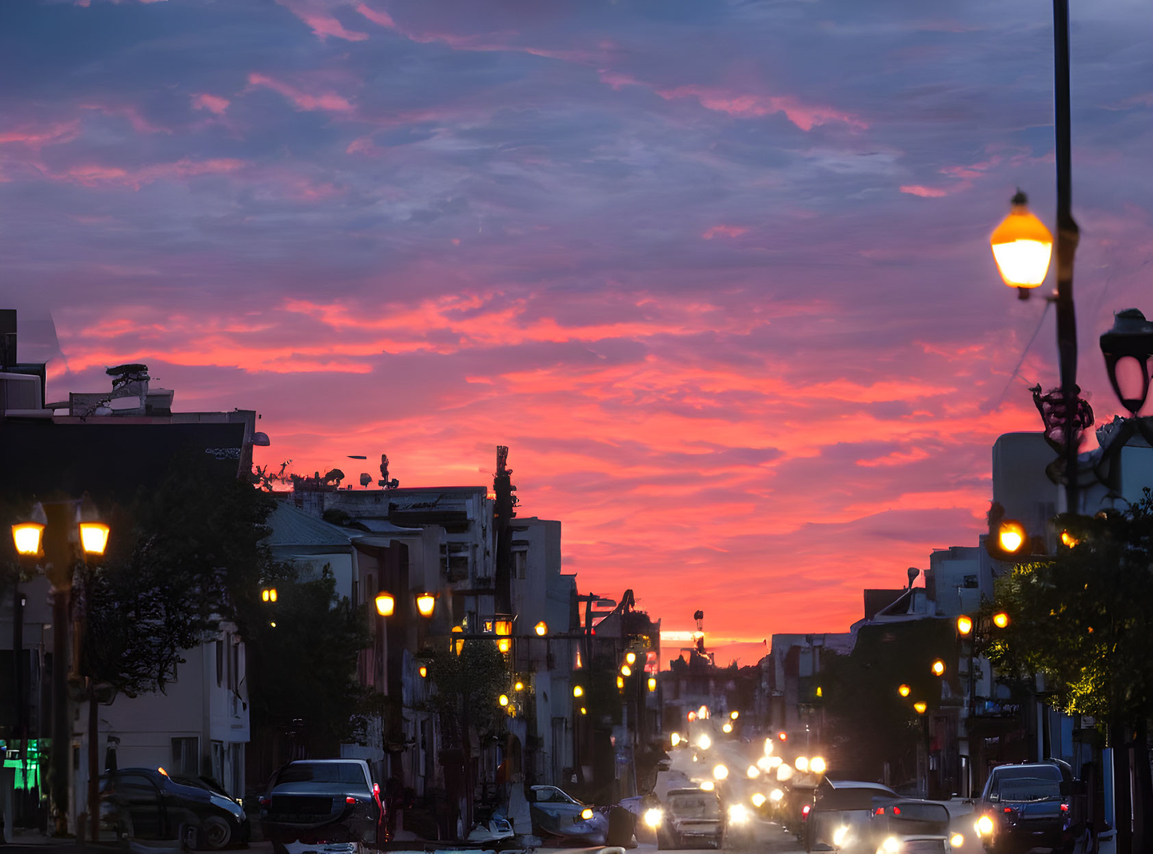 Vibrant pink and purple sunset over busy city street with cars and street lamps