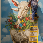 Artist painting vibrant multicolored goat on wall from ladder