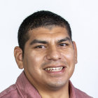 Young man portrait with olive skin and dark hair smiling subtly.