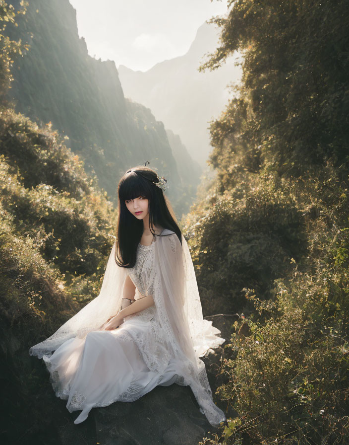 Long-haired person in white gown amidst greenery and mountains.