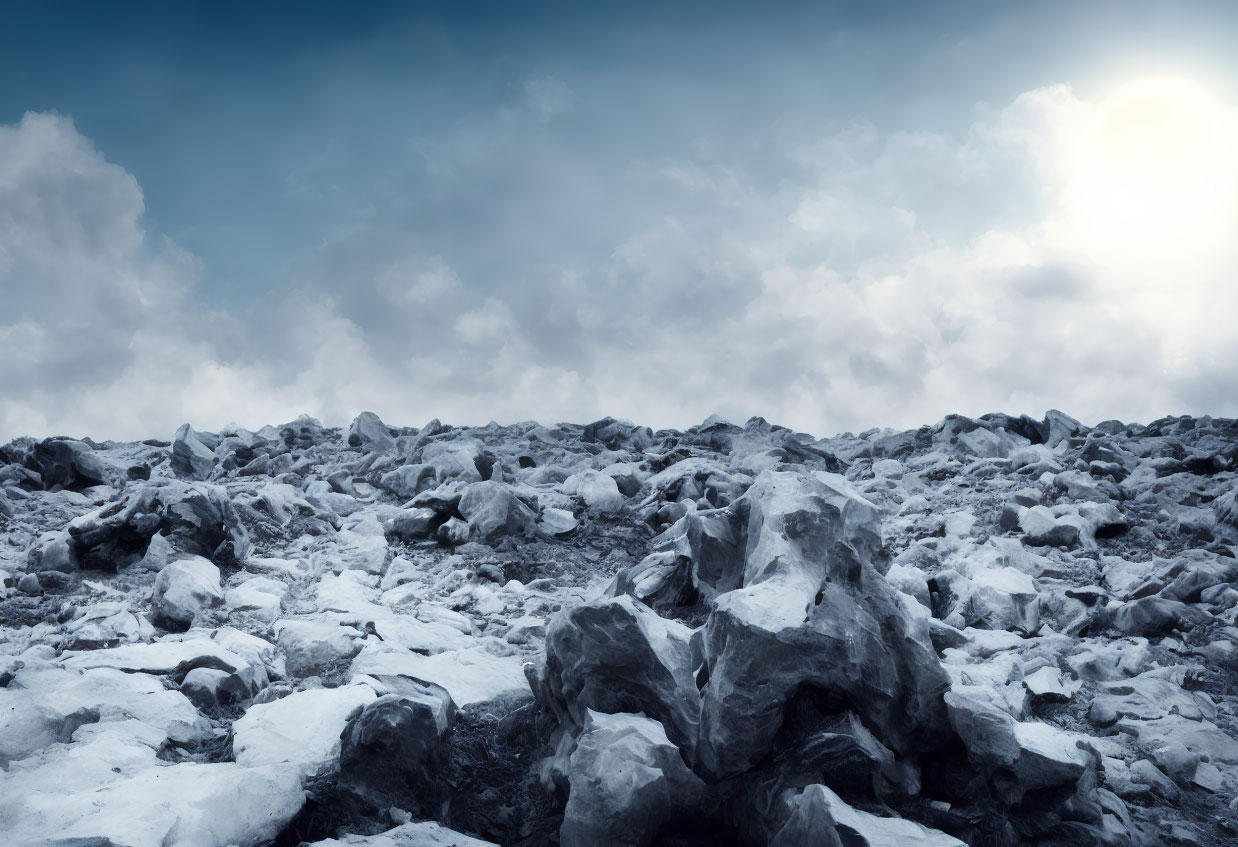 Snow-covered rocky terrain under cloudy sky with sun peeking through